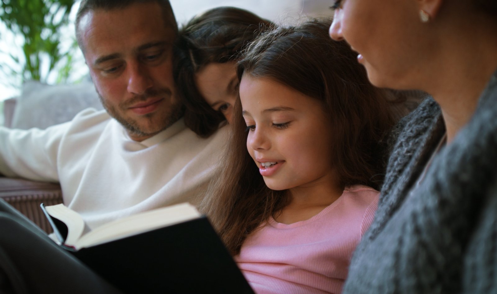 A father and mother reading Scripture together with their two daughters on the couch
