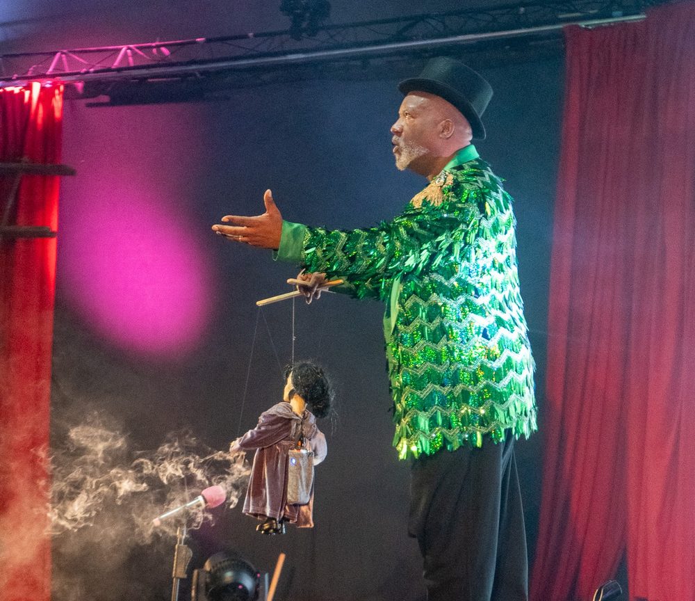 A puppeteer in a sequined green jacket performing on stage