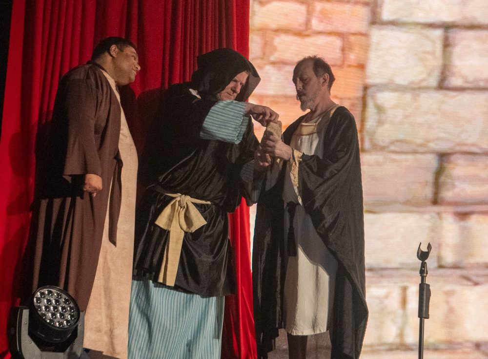 Three actors in robes reading from a scroll