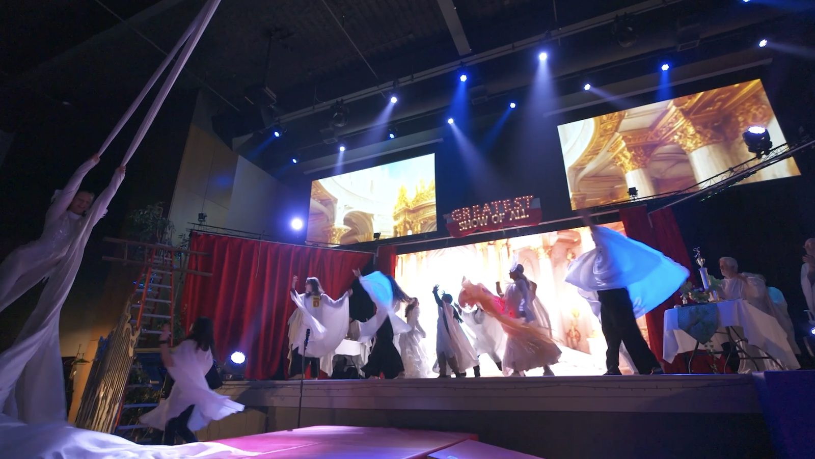 Cast members dancing with flowing fabric beneath aerial silks